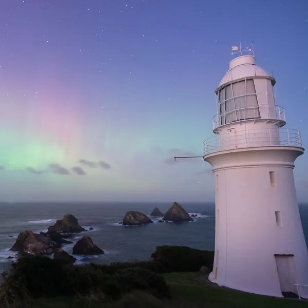 A strong display of the Aurora Australis still visible at first light beyond the Maatsuyker lighthouse and Needles